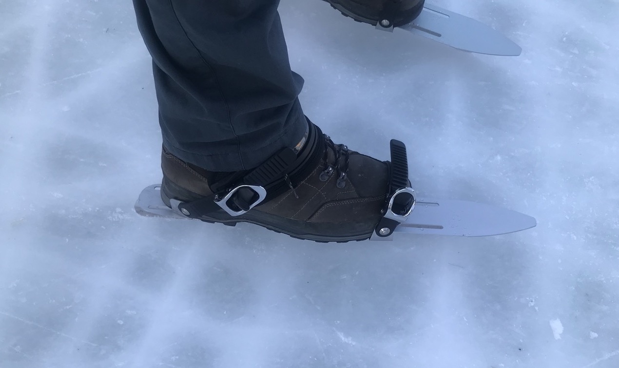 Foto: Ein Fuß mit Bergschuh, der auf Eislaufkufen geschnallt ist.