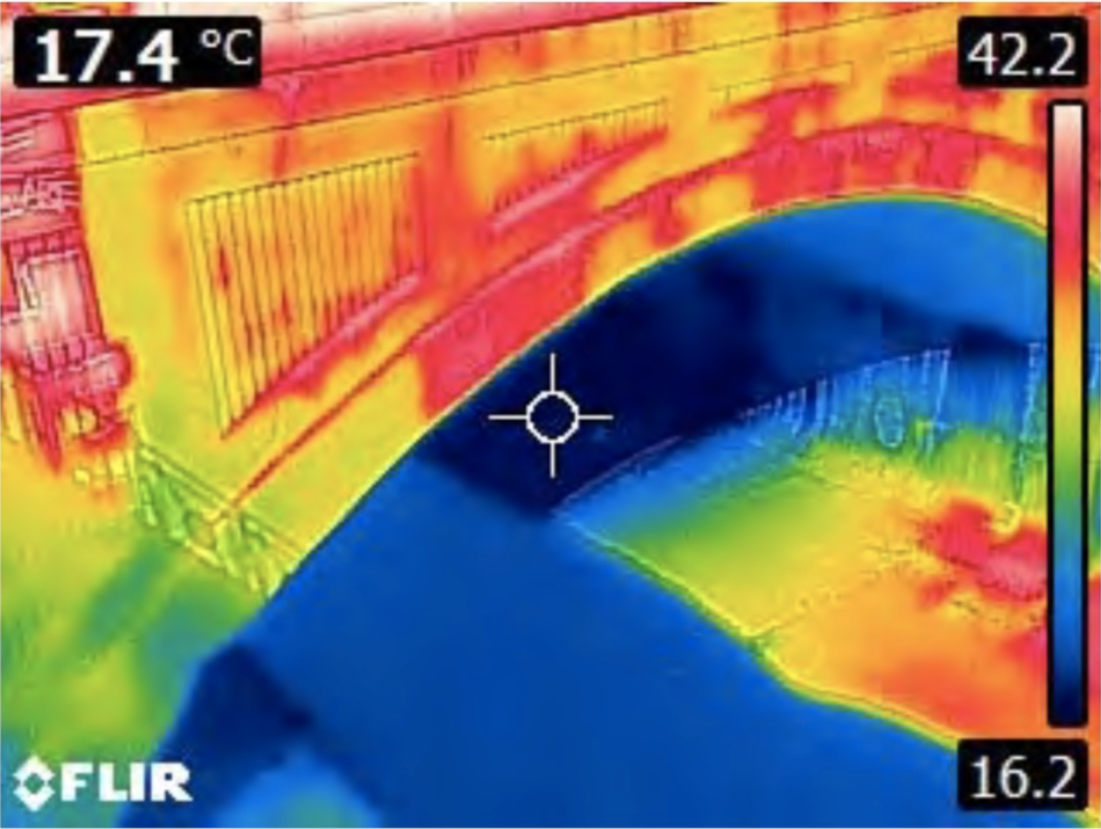 Thermalfoto: Brückenbogen in gelb/rot. Unter der Brücke eine große blaue Fläche.