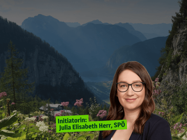 Porträt von Julia Herr, einer Frau mit langen braunen Haaren und Brille, vor einem abgedunkelten Alpental mit Bergwald und rosa Blüten im Vordergrund, darauf ein grünes Etikett »Initiatorin: Julia Elisabeth Herr, SPÖ«